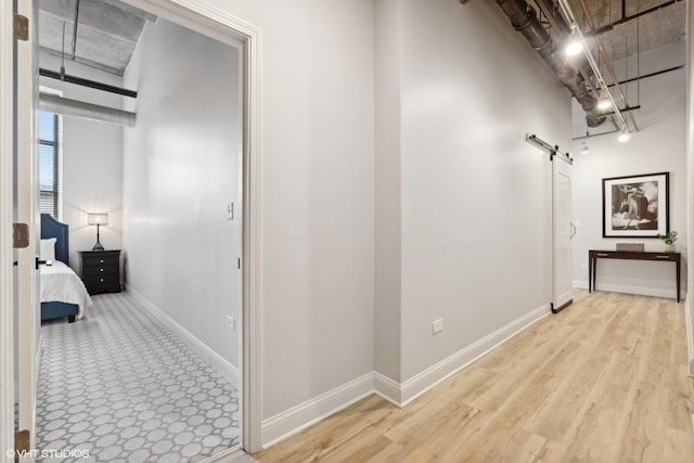 hallway featuring light wood-style floors, a barn door, and baseboards