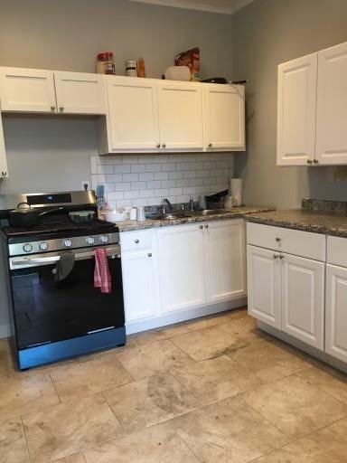 kitchen featuring white cabinets, backsplash, sink, and stainless steel range oven