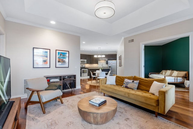 living room featuring wood-type flooring, a raised ceiling, and crown molding