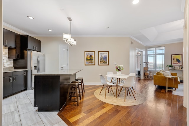 kitchen featuring a kitchen breakfast bar, stainless steel fridge, crown molding, pendant lighting, and a kitchen island