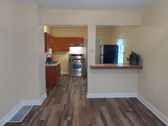 kitchen featuring dark wood-type flooring, sink, decorative backsplash, fridge, and gas stove