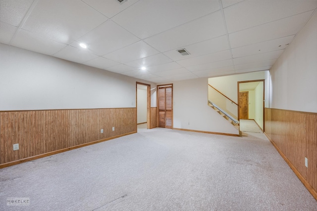 carpeted spare room featuring a drop ceiling and wooden walls