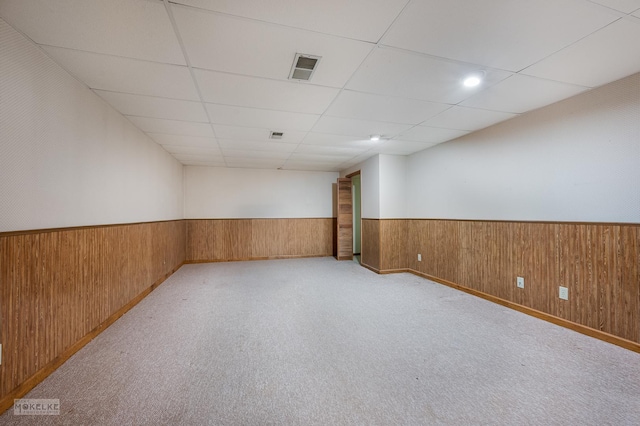 spare room featuring a paneled ceiling, wooden walls, and light carpet