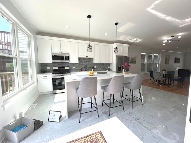 kitchen with a kitchen breakfast bar, hanging light fixtures, appliances with stainless steel finishes, a kitchen island, and white cabinetry