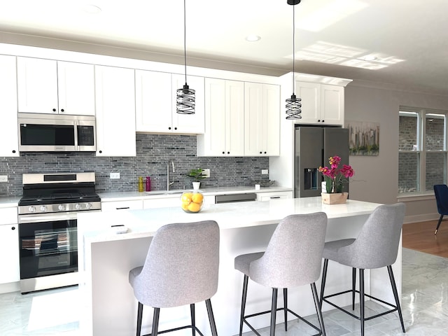 kitchen with a center island, decorative light fixtures, a kitchen bar, white cabinetry, and stainless steel appliances