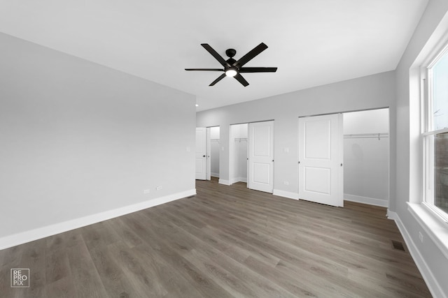 unfurnished bedroom with multiple windows, ceiling fan, dark wood-type flooring, and two closets