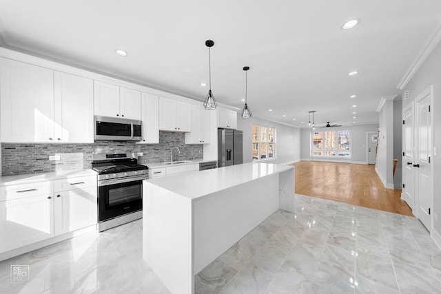 kitchen with white cabinetry, ceiling fan, stainless steel appliances, crown molding, and a kitchen island