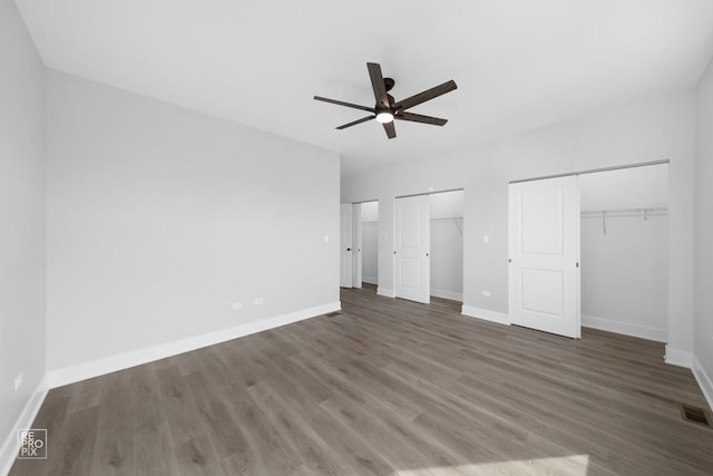 unfurnished bedroom featuring ceiling fan, dark hardwood / wood-style floors, and multiple closets