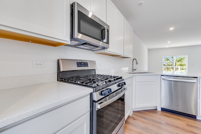 kitchen featuring sink, appliances with stainless steel finishes, light hardwood / wood-style floors, light stone counters, and white cabinetry