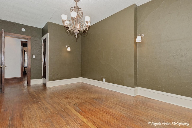 spare room featuring wood-type flooring and a notable chandelier