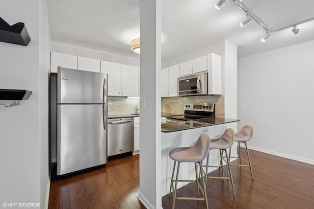 kitchen with a kitchen bar, tasteful backsplash, stainless steel appliances, dark wood-type flooring, and white cabinetry