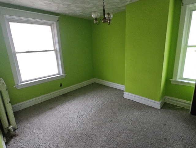 unfurnished room featuring radiator heating unit, a textured ceiling, plenty of natural light, and a notable chandelier