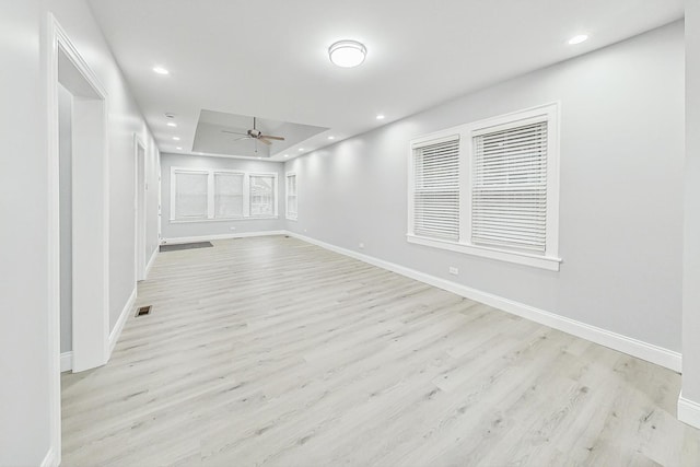 empty room featuring a raised ceiling, light hardwood / wood-style flooring, and ceiling fan