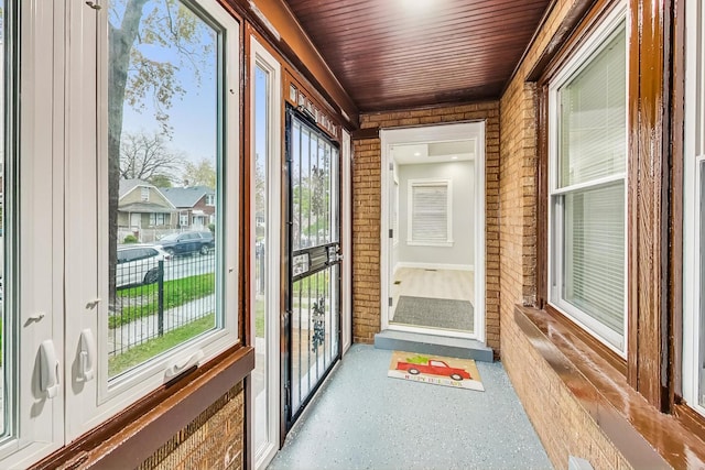 doorway featuring wood ceiling, a healthy amount of sunlight, and brick wall