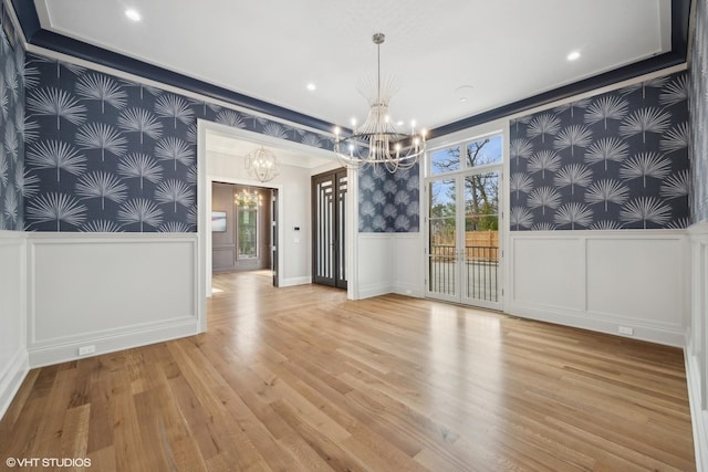 unfurnished dining area with a wainscoted wall, crown molding, a notable chandelier, wood finished floors, and wallpapered walls