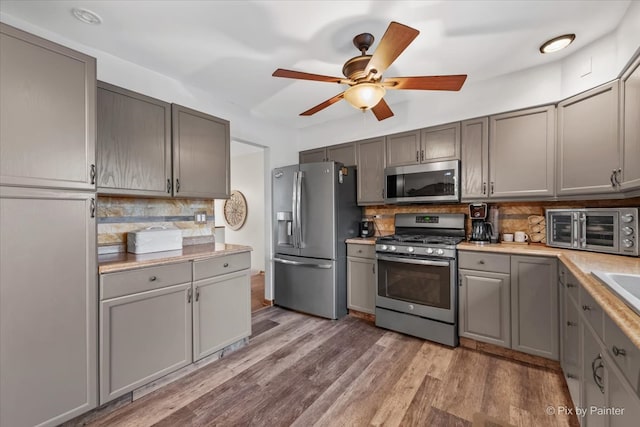 kitchen featuring backsplash, gray cabinetry, stainless steel appliances, and hardwood / wood-style flooring