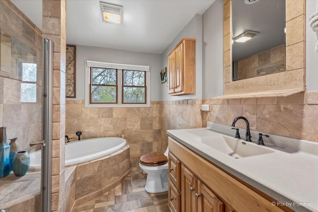 bathroom featuring vanity, tiled bath, toilet, and tile walls