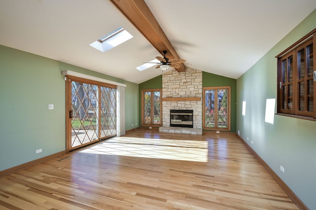 unfurnished living room featuring light hardwood / wood-style floors, a stone fireplace, ceiling fan, and lofted ceiling with skylight