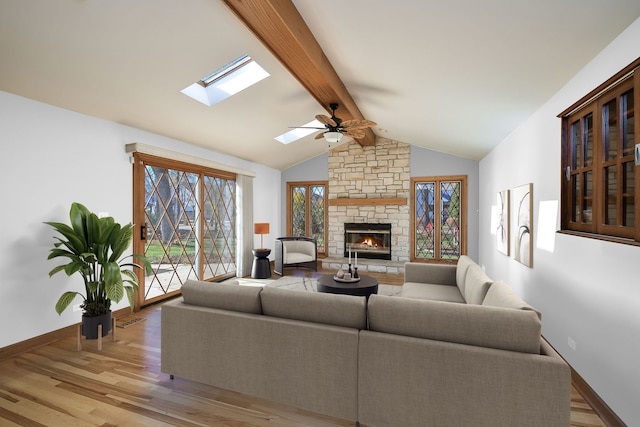 living room with vaulted ceiling with skylight, ceiling fan, light hardwood / wood-style floors, and a fireplace