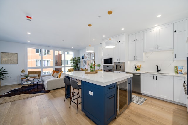 kitchen with white cabinetry, sink, stainless steel appliances, light hardwood / wood-style flooring, and pendant lighting