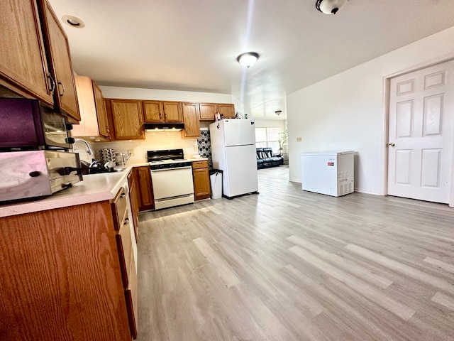 kitchen with decorative backsplash, light wood-type flooring, white appliances, and sink