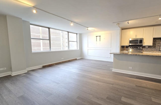 kitchen featuring white cabinets, dark wood finished floors, decorative backsplash, dark stone countertops, and stainless steel appliances