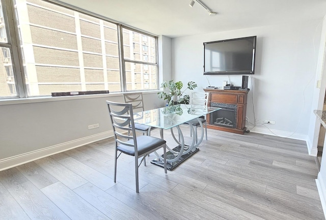 dining room featuring rail lighting, a fireplace, baseboards, and wood finished floors