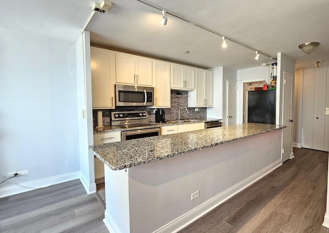 kitchen featuring light wood finished floors, stainless steel appliances, backsplash, a sink, and light stone countertops