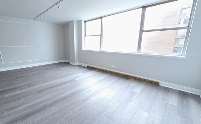 empty room featuring baseboards, wood finished floors, and track lighting