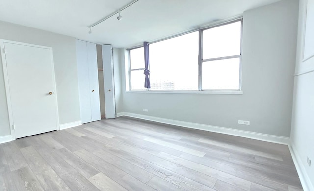 unfurnished room with track lighting, light wood-type flooring, and baseboards