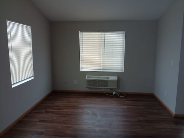 spare room featuring a wall unit AC, dark hardwood / wood-style flooring, and vaulted ceiling