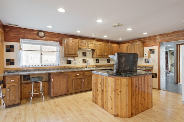 kitchen with a kitchen breakfast bar, wooden walls, sink, light hardwood / wood-style floors, and a kitchen island