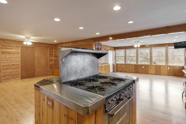 kitchen with stainless steel counters, light hardwood / wood-style flooring, ceiling fan, and wood walls