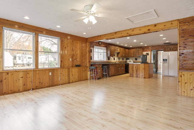 kitchen with a center island, white refrigerator with ice dispenser, wooden walls, light hardwood / wood-style flooring, and ceiling fan