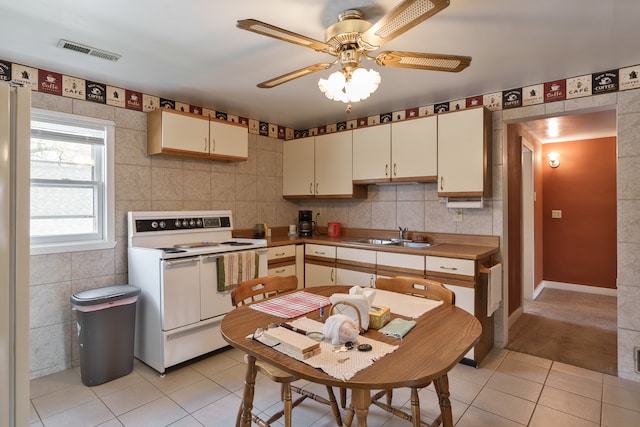 kitchen with cream cabinetry, sink, light tile patterned floors, and white electric stove