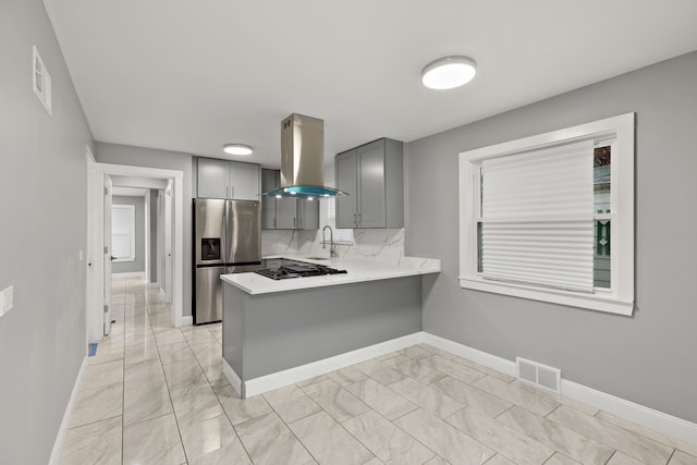 kitchen featuring backsplash, wall chimney range hood, gray cabinets, appliances with stainless steel finishes, and kitchen peninsula