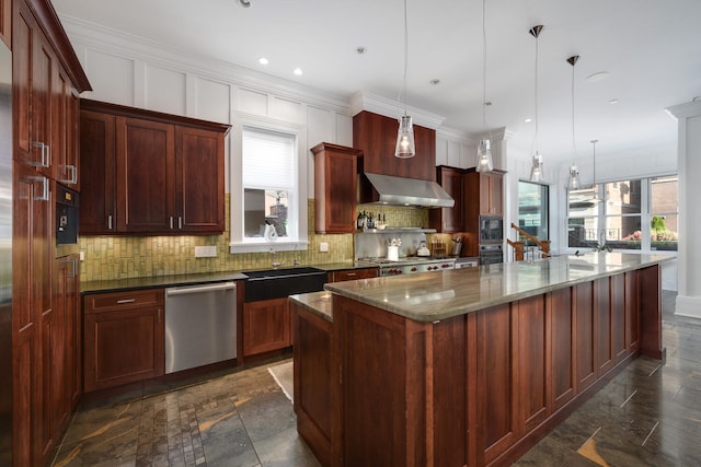 kitchen featuring wall chimney exhaust hood, dark stone countertops, pendant lighting, a center island with sink, and appliances with stainless steel finishes