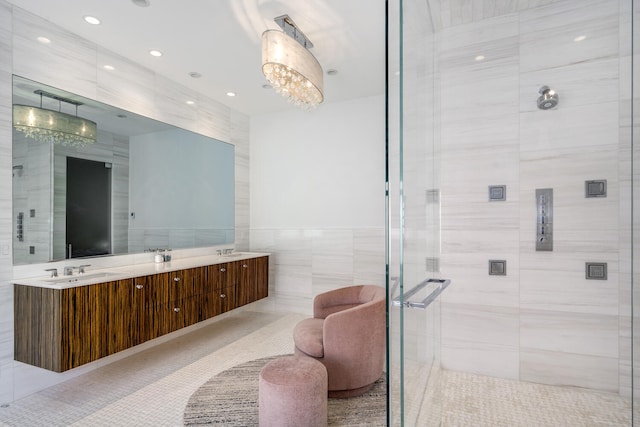 bathroom featuring an inviting chandelier, tile patterned floors, a shower with door, vanity, and tile walls