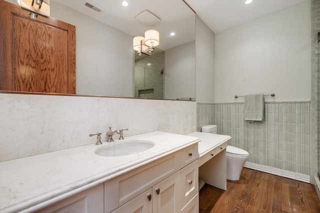 bathroom featuring wood-type flooring, toilet, vanity, a shower with shower door, and tile walls