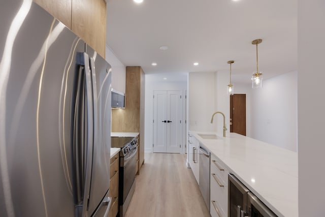 kitchen featuring light stone countertops, sink, light hardwood / wood-style flooring, pendant lighting, and appliances with stainless steel finishes