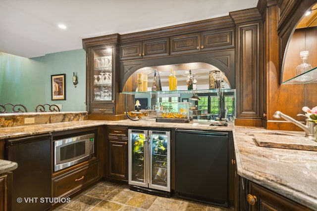 bar with dark brown cabinetry, stainless steel microwave, sink, wine cooler, and light stone counters