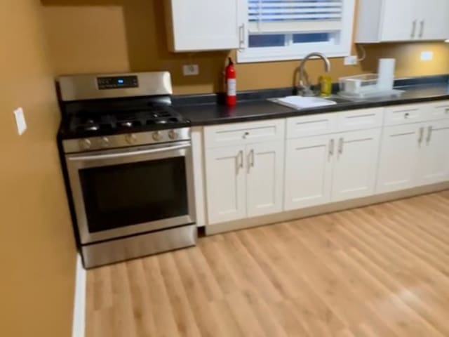 kitchen with light hardwood / wood-style floors, white cabinetry, stainless steel range with gas cooktop, and sink