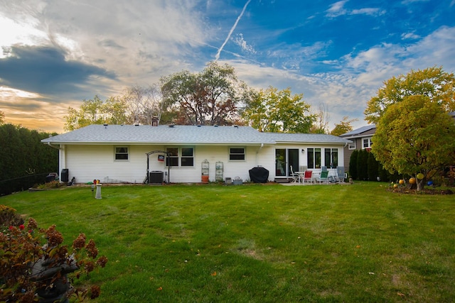 back house at dusk featuring central AC unit, a yard, and a patio