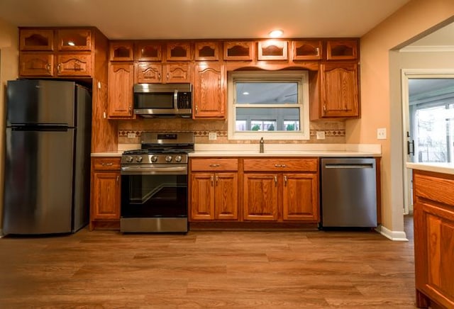 kitchen with stainless steel appliances, tasteful backsplash, sink, and light wood-type flooring