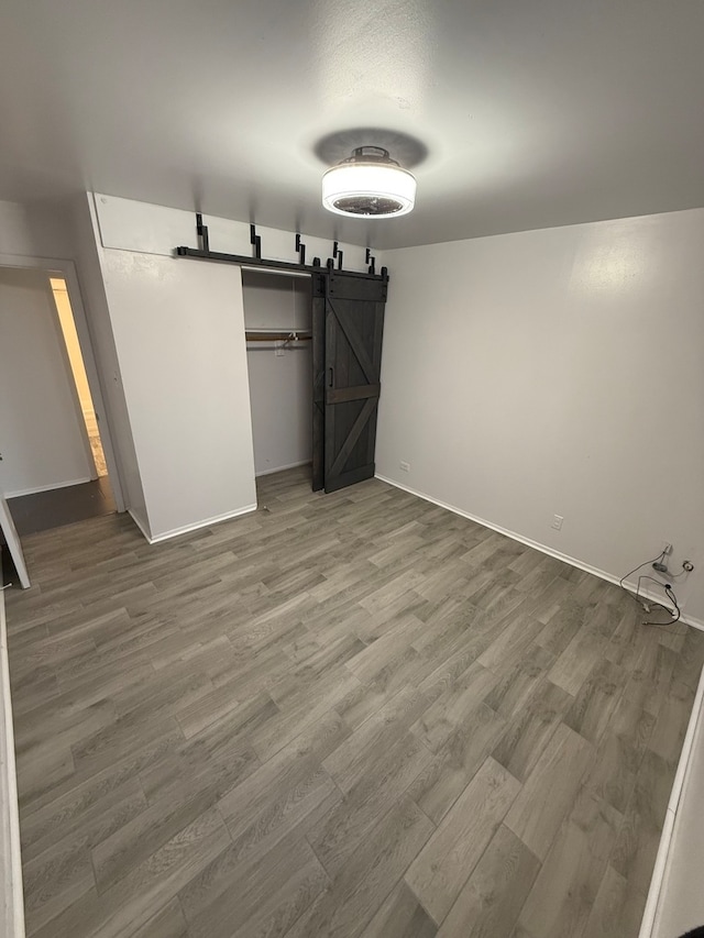 unfurnished bedroom with a barn door, a closet, and hardwood / wood-style flooring