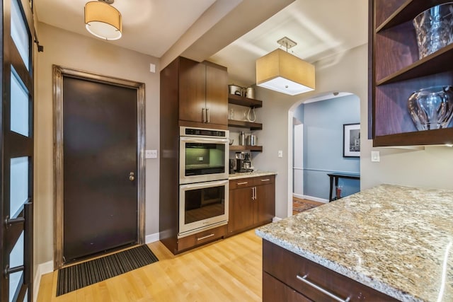 kitchen featuring light stone counters, open shelves, light wood finished floors, double oven, and arched walkways