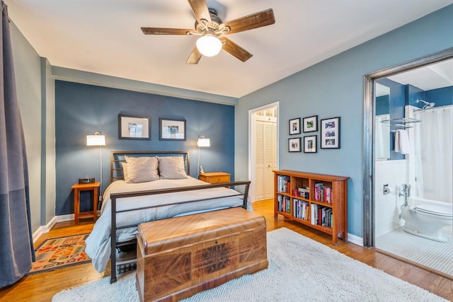 bedroom featuring ensuite bath, baseboards, ceiling fan, and wood finished floors