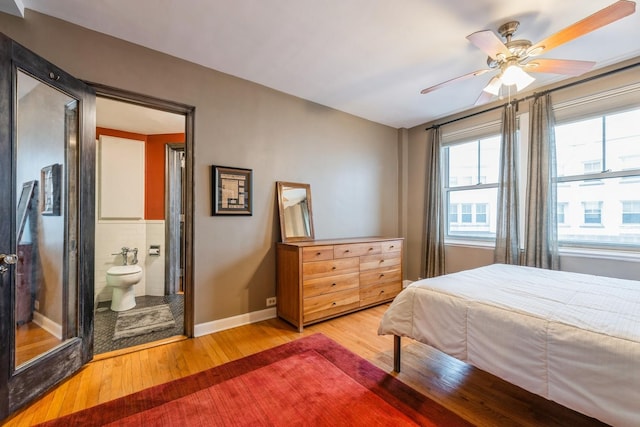 bedroom with a ceiling fan, wood finished floors, ensuite bathroom, baseboards, and tile walls