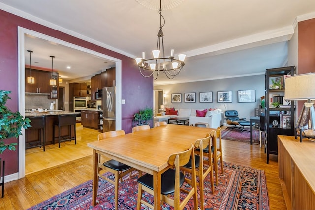 dining area featuring an inviting chandelier, ornamental molding, and light wood-type flooring
