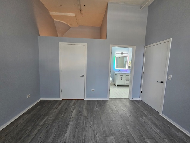 unfurnished bedroom featuring ensuite bathroom, dark hardwood / wood-style flooring, and a towering ceiling